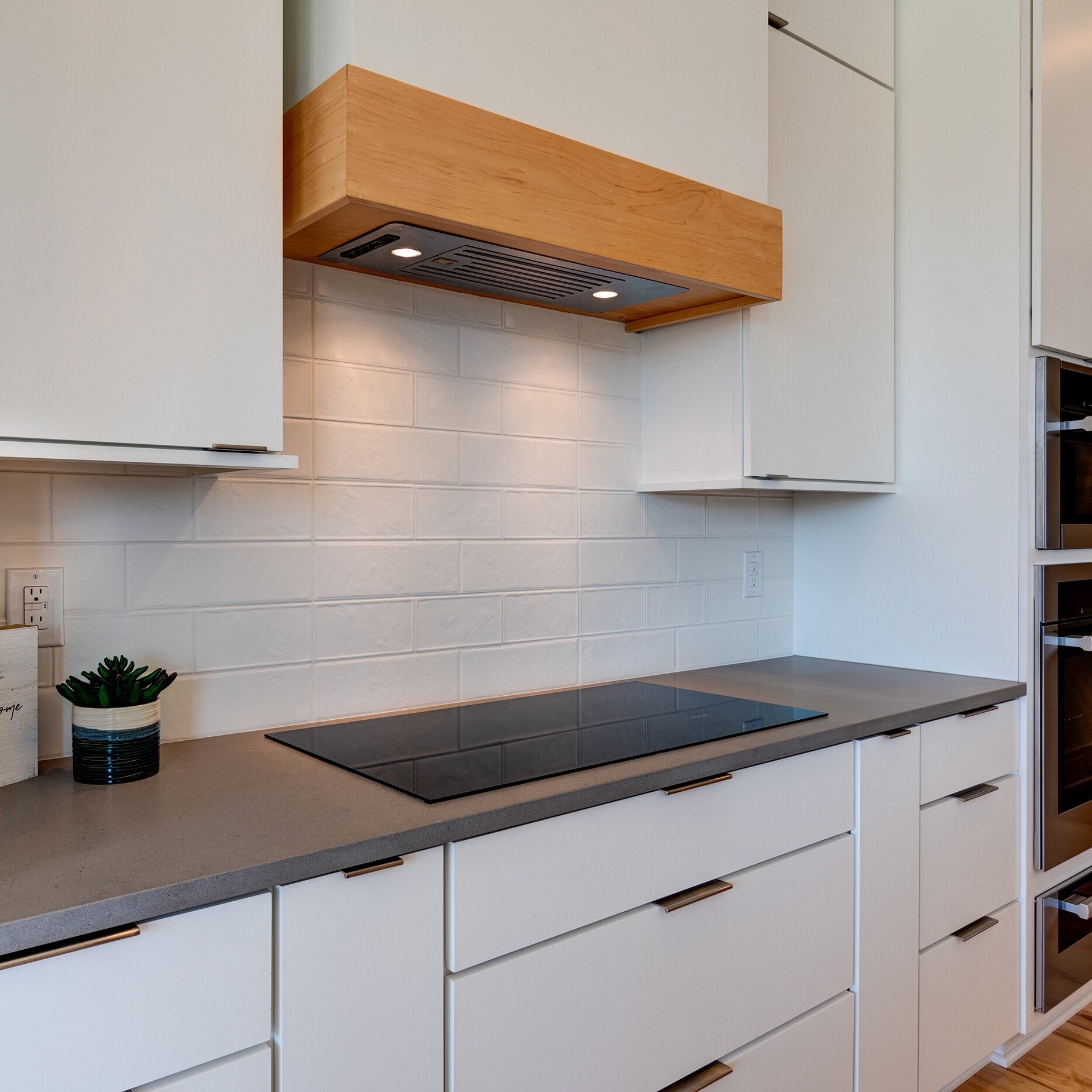 A kitchen with white cabinets and wood floors.