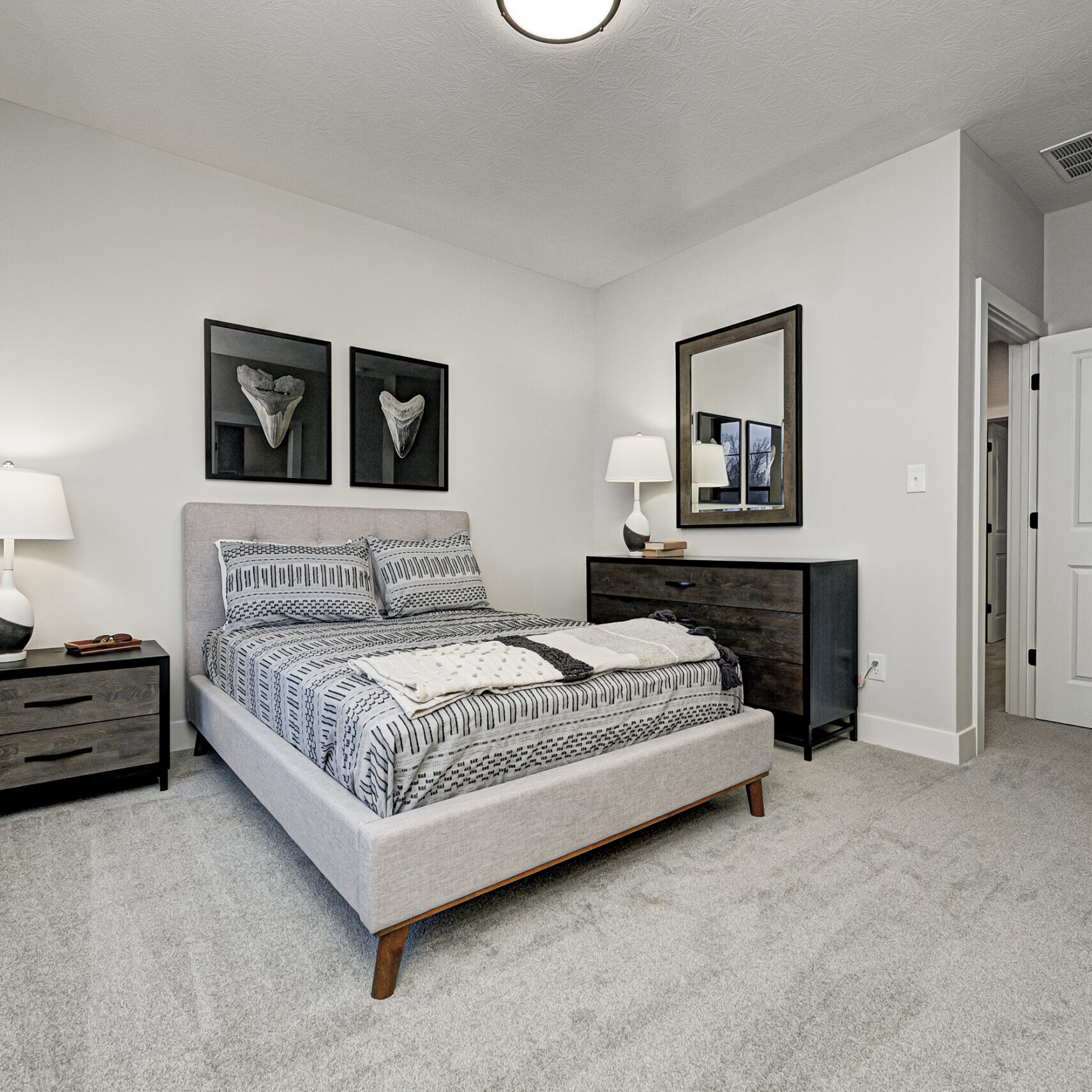 A bedroom with a bed, dresser and mirror in a custom home.