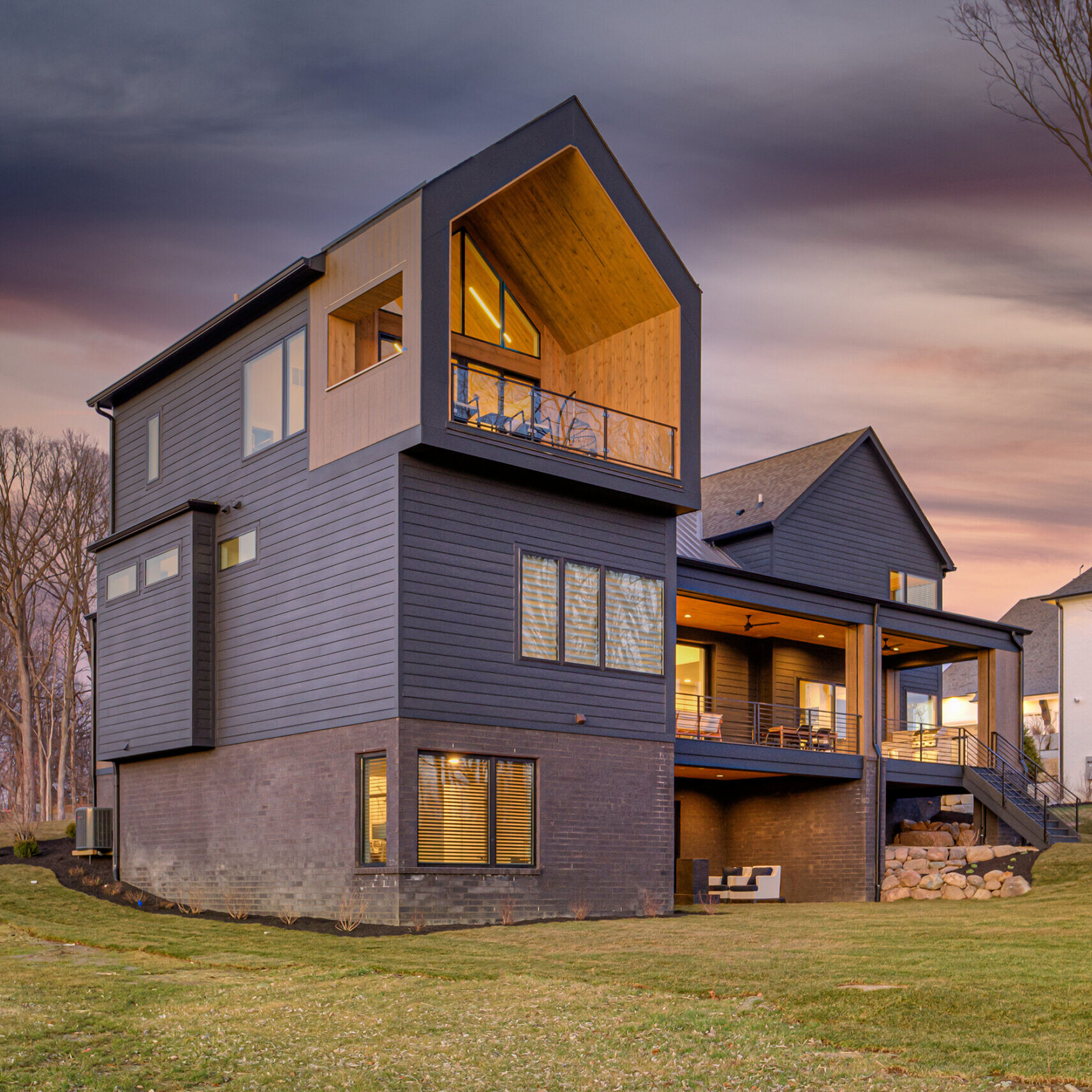 A black house with a deck and a grassy yard.