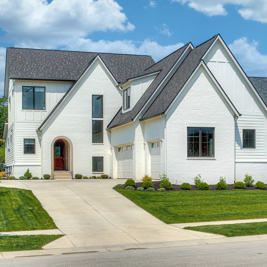 A white house with a green lawn and a driveway.
